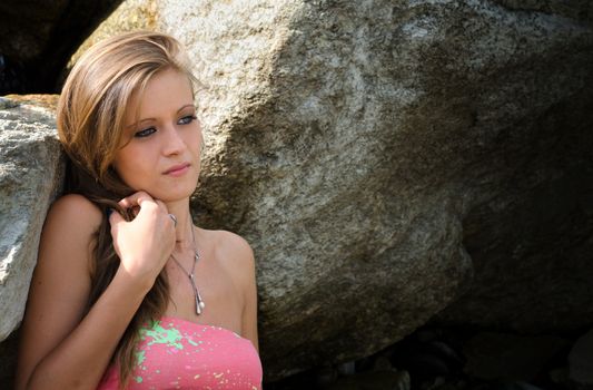 Pretty blue eyed, brunette girl in bikini against rocks looking away