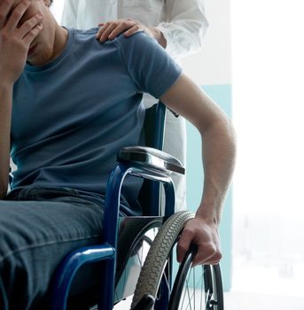 Female doctor consoling sad man sitting in wheelchair