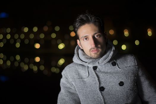 Attractive young man portrait at night with city lights behind him, looking at camera