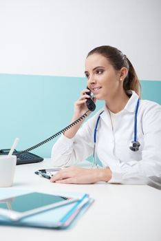 Young female doctor sitting at her desk and talking on the phone