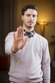 Handsome, seerious young man doing stop sign with his hand with a severe expression. 