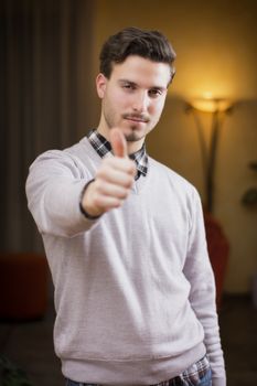 Attractive young man with thumb up doing OK sign, indoor shot inside a house