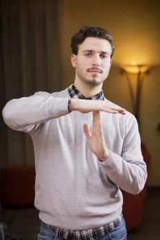 Attractive young man doing time-out sign, indoor shot inside a house