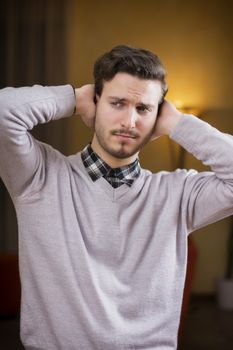Handsome young man covering his ears, stressed or unhappy because of too much noise. Indoors shot