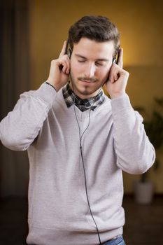 Attractive young man listening to music on headphones, eyes closed. Indoor shot in house