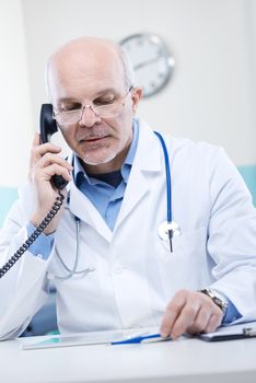 Doctor talking on the phone and holding a thermometer.