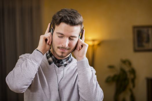 Attractive young man listening to music on headphones, eyes closed. Indoor shot in house