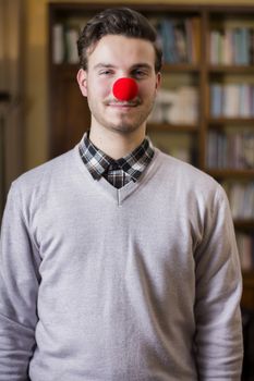Handsome young man smiling with red clown nose, standing in a living room
