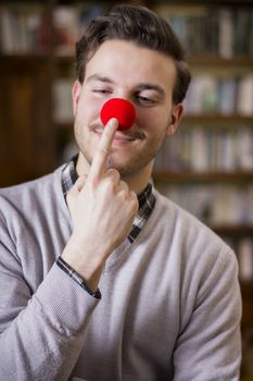 Handsome young man smiling and touching red clown nose, standing in a living room