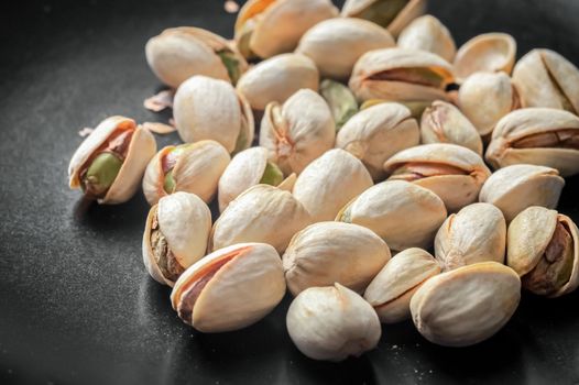 closeup of lightly roasted pistachio nuts in a black bowl