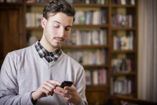 Attractive young man typing on cell phone, indoor shot in house living room