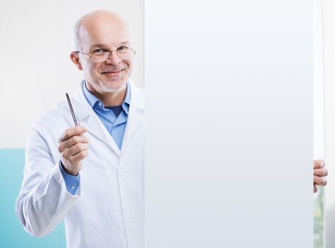 Senior doctor holding a big white sign and pointing with a pen, blank copy space.