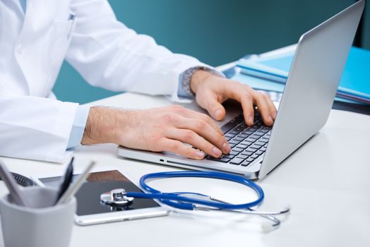 Doctor working at his desk with stethoscope, laptop and tablet.