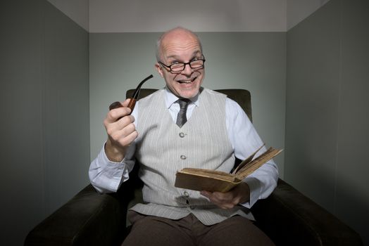 Senior cheerful man reading in armchair and smoking pipe.