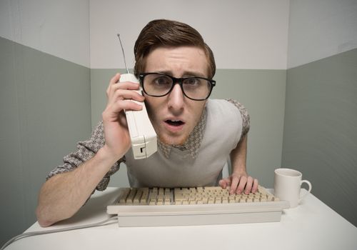 Vintage nerd guy talking on the phone and typing.