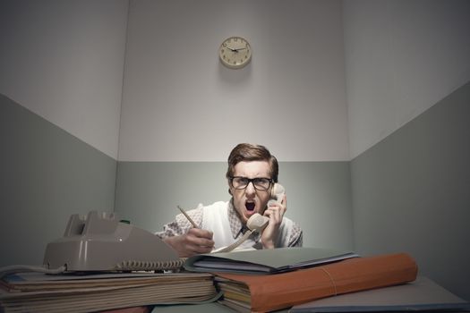 Angry nerd guy at the phone with messy desk.