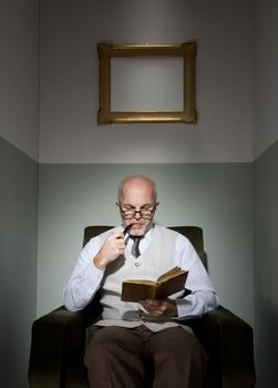 Senior handsome man reading in armchair and smoking pipe.