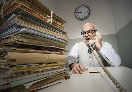 Vintage senior businessman on the phone with a huge stack of files.