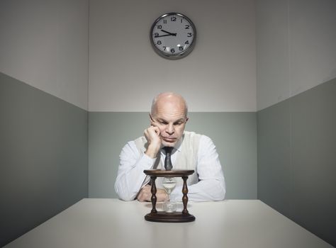 Bored vintage businessman waiting at desk with hourglass.