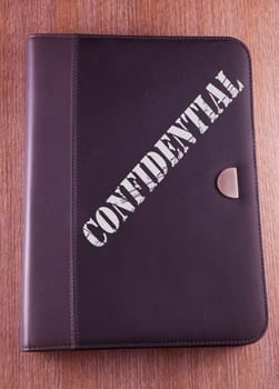 Gray folder over wooden background, with text "Confidential" over it