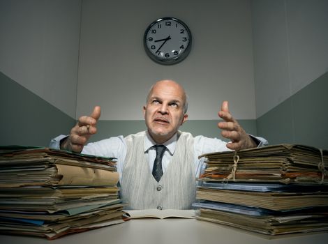 Angry office worker with piles of folders in a small room.
