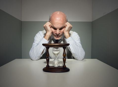 Bored vintage businessman waiting at desk with hourglass.