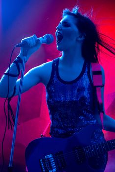 Young teenager rock star singing and playing electric guitar on stage.