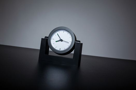 Modern black clock on black table in the office. Gray background.