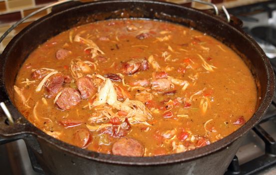 Chicken and sausage gumbo cooking in an iron kettle.