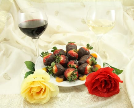A glass of red and white wine with chocolate covered strawberries, chocolate covered apricots and roses.