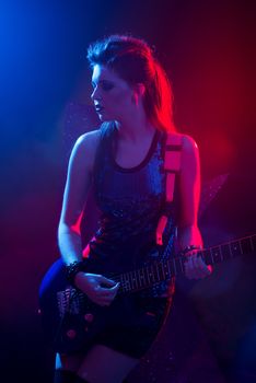 Young teenager rock star singing and playing electric guitar on stage.