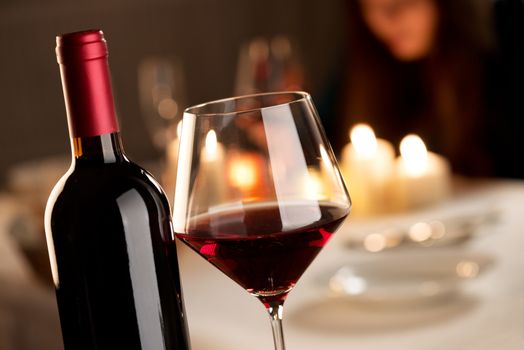 Bottle and glass of red wine with restaurant on background.