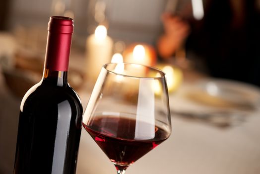 Bottle and glass of red wine with restaurant on background.