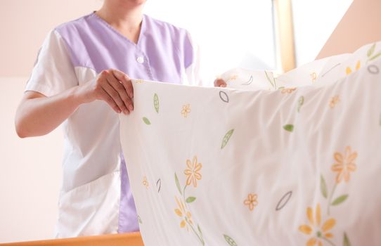 Woman making bed and changing bedding in guest room.