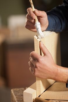 Professional carpenter applying glue on a wooden surface with brush.