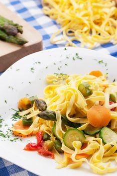 Traditional tagliatelle with summer vegetables on checkered tablecloth.