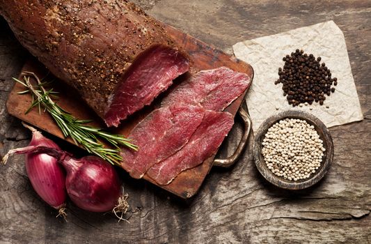 Slices of meat with spices and onions on wooden board.