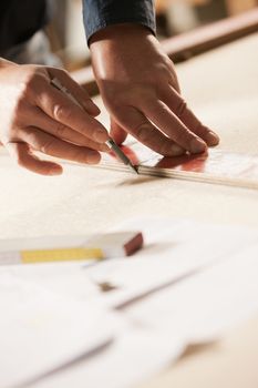 Carpenter measuring and tracing lines with a ruler on a wooden surface.