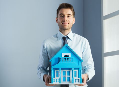 Friendly real estate agent with light blue model house.