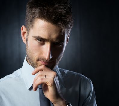 Young confident businessman looking at camera and touching his chin.