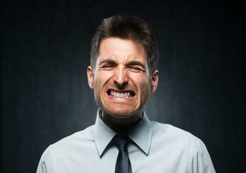 Furious young businessman on dark gray background.