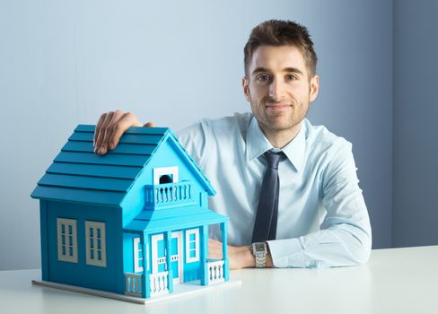 Friendly real estate agent with light blue model house.