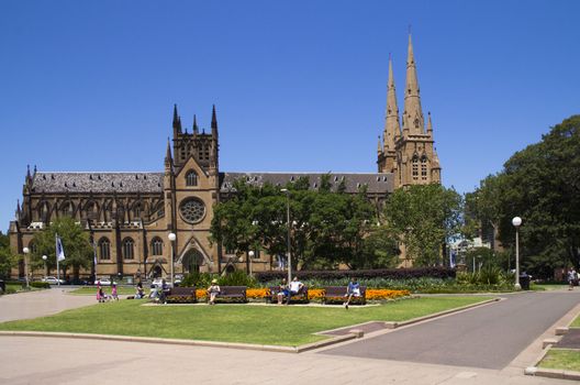 SYDNEY, AUSTRALIA-December 19th 2913: People relaxing in Hyde park next to St Andrew's Cathedral. Built in Gothic Revival style and consecrated in 1868, the cathedral is the oldest in Australia.