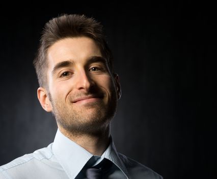 Attractive young businessman looking at camera and smiling on dark background.