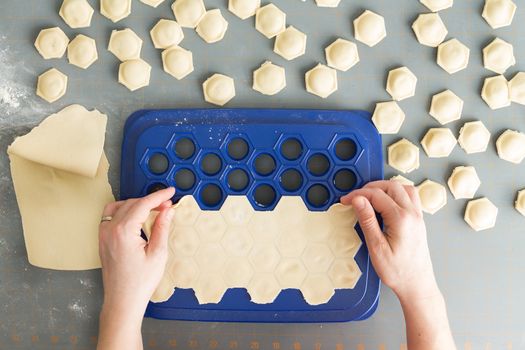 Overhead view of a woman preparing ravioli from fresh dough as she forms decorative hexagonal casings with a savory filling of this traditional Italian pasta