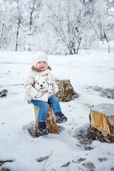 Little girl sat down on a stump in the winter forest