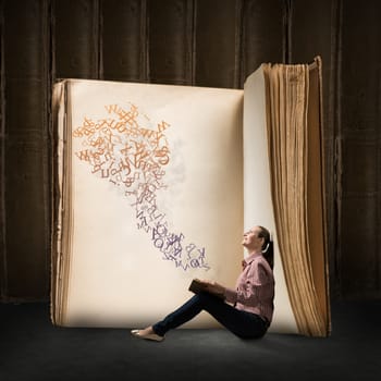 image of a young woman reading a book sitting near a big book