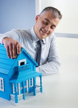 Real estate agent at desk with light blue model house.