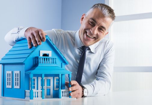 Real estate agent at desk with light blue model house.