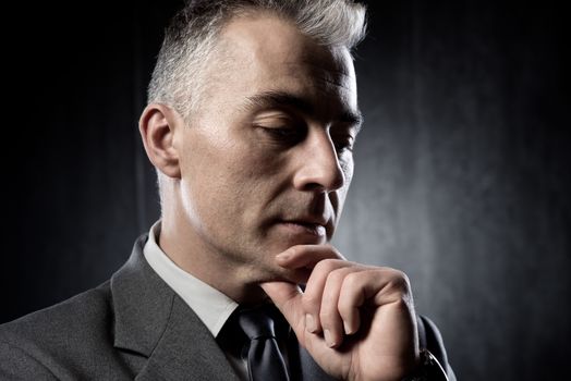 Pensive businessman with hand on chin on dark background.